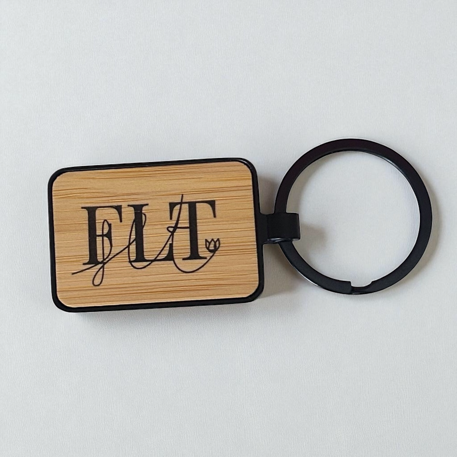 Porte-clés rectangulaire en bois de bambou et métal noir, avec logo FLT gravé au laser.
